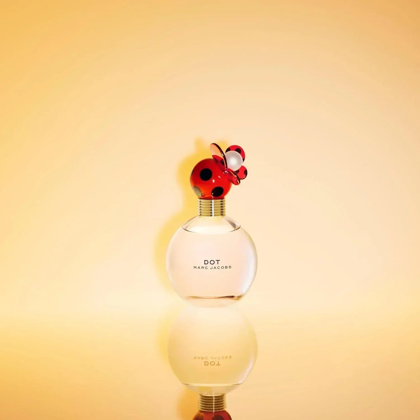 Marc Jacobs Dot Eau de Parfum bottle with ladybird cap on reflective surface
