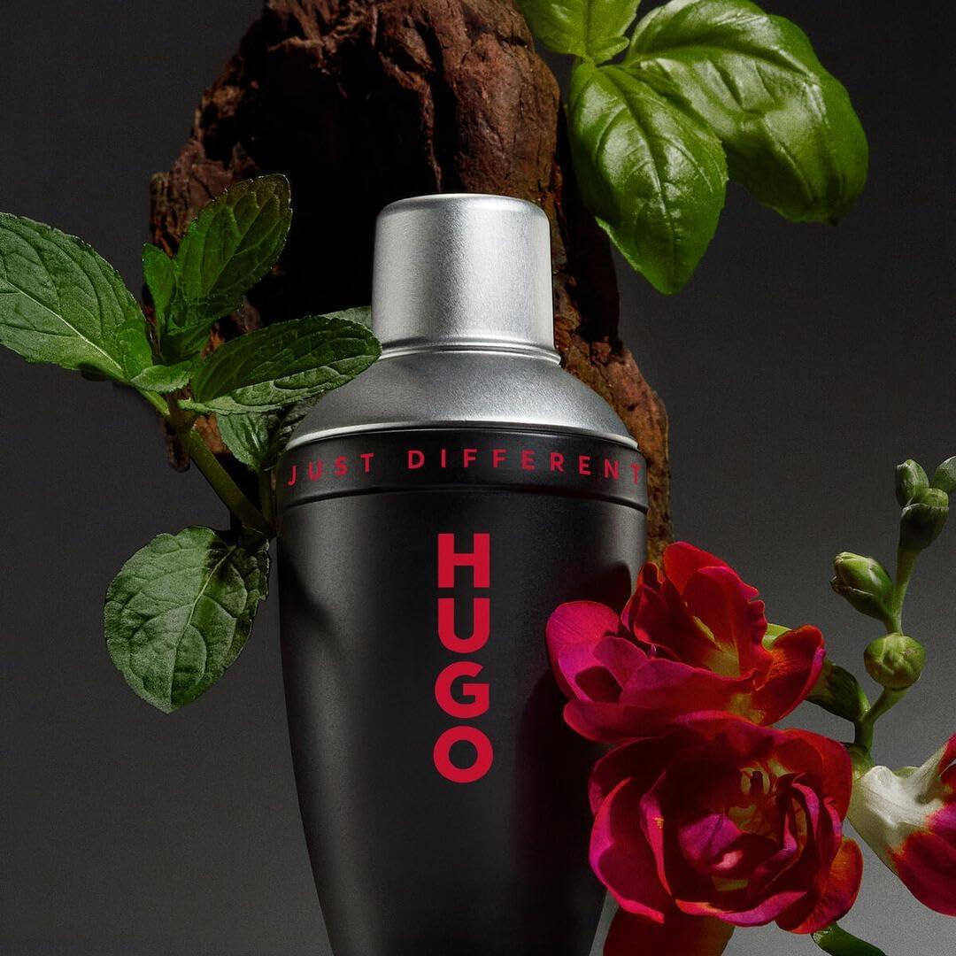 Black Hugo perfume bottle with red text, surrounded by green leaves and flowers on a dark background