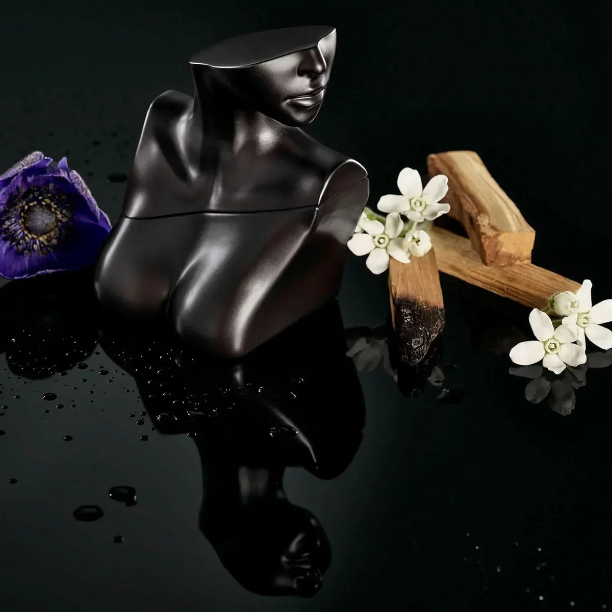 Black sculptural fragrance bottle with purple flower and white blooms on dark reflective surface