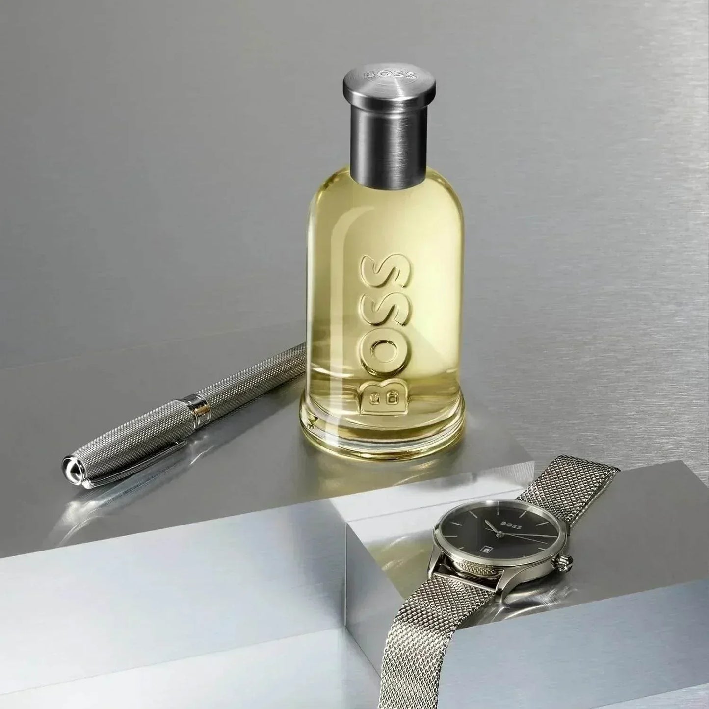 BOSS Bottled Eau de Toilette fragrance bottle with pen and watch on metallic surface
