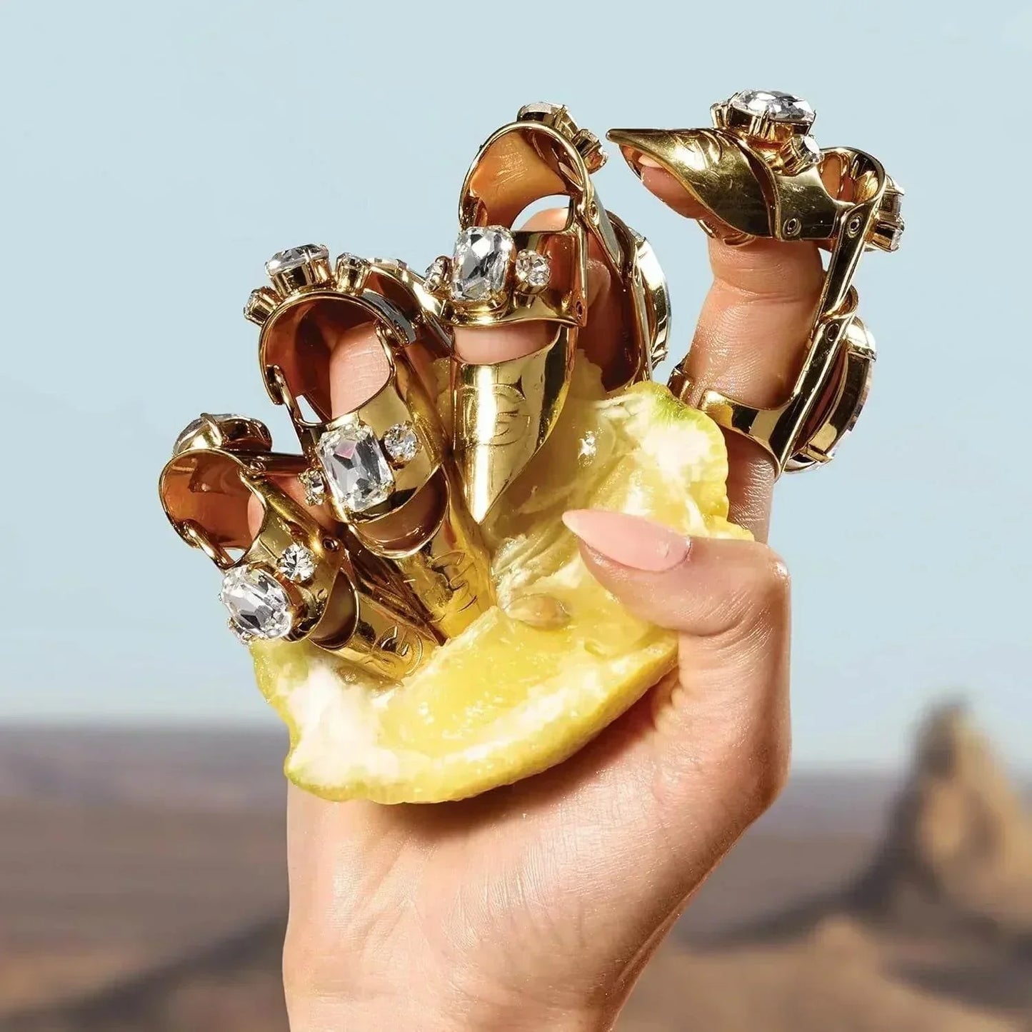 Hand holding lemon slice with gold jeweled rings on fingers