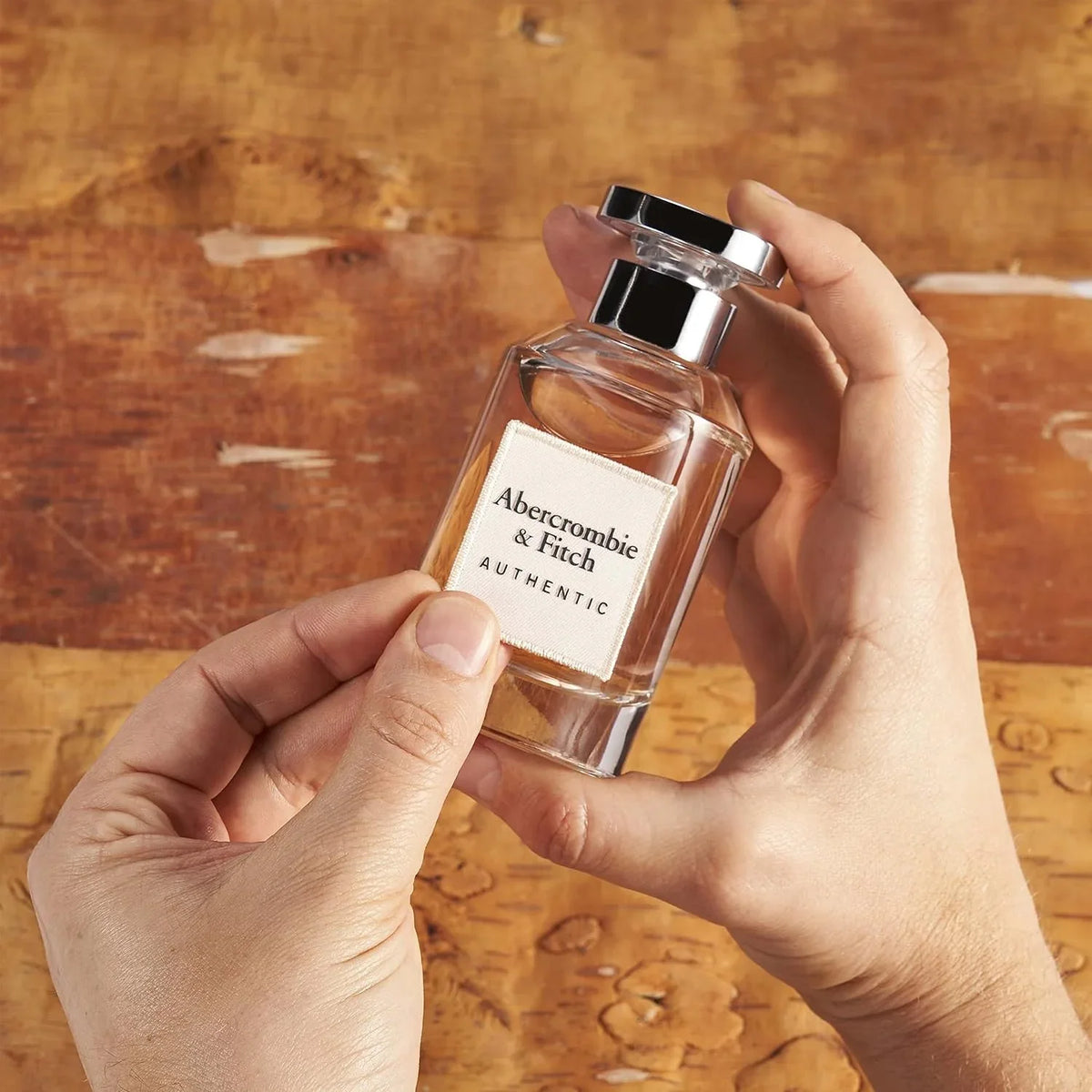 Hand holding a Abercrombie & Fitch perfume bottle on a wooden surface