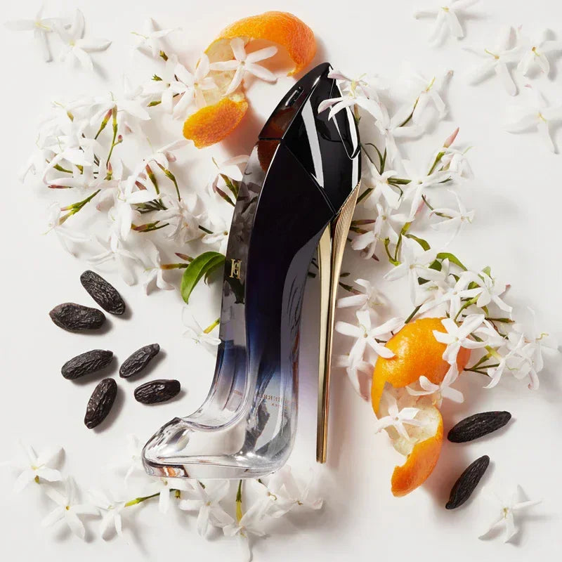 High heel perfume bottle with white flowers, orange peels, and tonka beans on white background