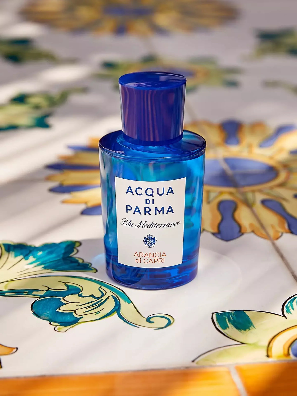 A bottle of Acqua di Parma Blu Mediterraneo Eau de Toilette with a blue cap and a white label, set on a decorative Mediterranean tile surface.