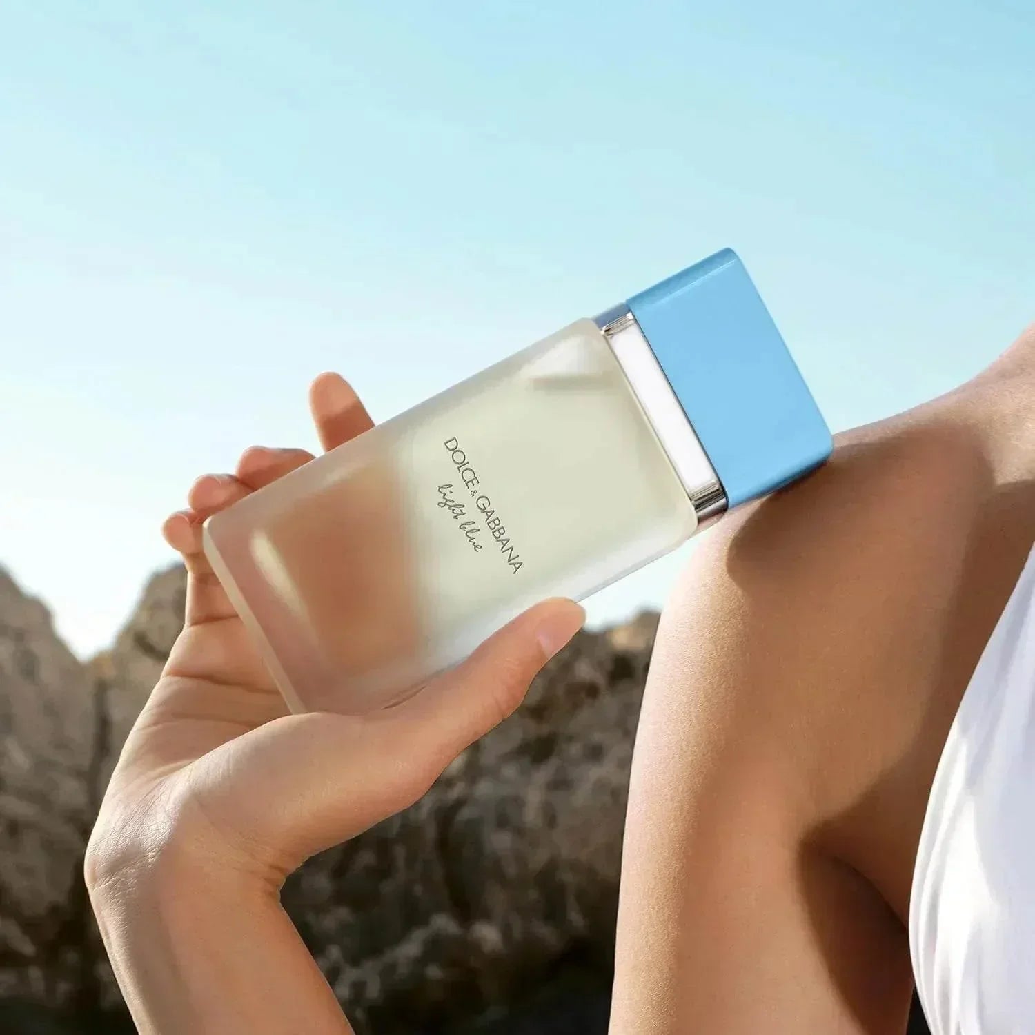 Dolce & Gabbana Light Blue fragrance bottle held against sunny sky