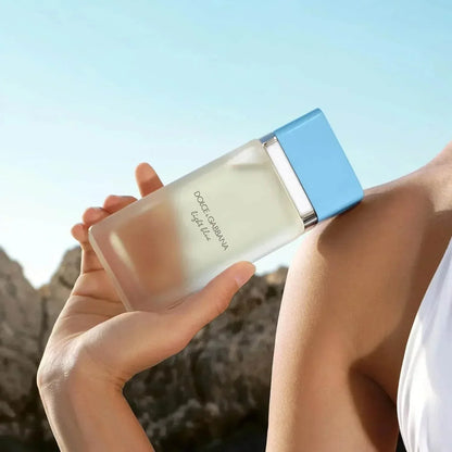 Dolce & Gabbana Light Blue fragrance bottle held against sunny sky