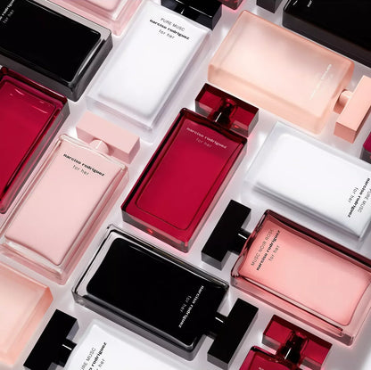 An overhead flat-lay arrangement of rectangular perfume bottles in translucent shades of black, white, blush pink, and deep red, with small white cards displaying text between them.
