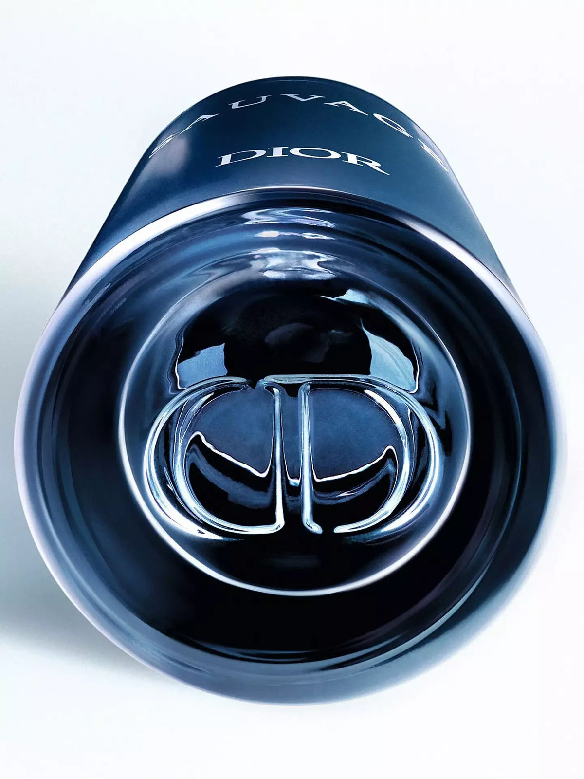 Close-up of a glossy dark blue Dior Sauvage bottle showing the embossed silver-toned Dior logo and part of the white DIOR and SAUVAGE text on a clean white background.