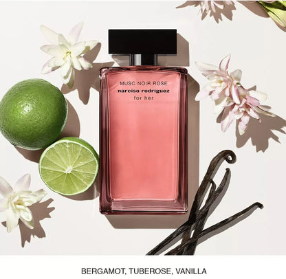 A rectangular pink perfume bottle labeled 'MUSC NOIR ROSE narciso rodriguez for her' is arranged on a white background with a lime, white flowers, vanilla beans, and a text banner at the bottom reading 'BERGAMOT, TUBEROSE, VANILLA'.