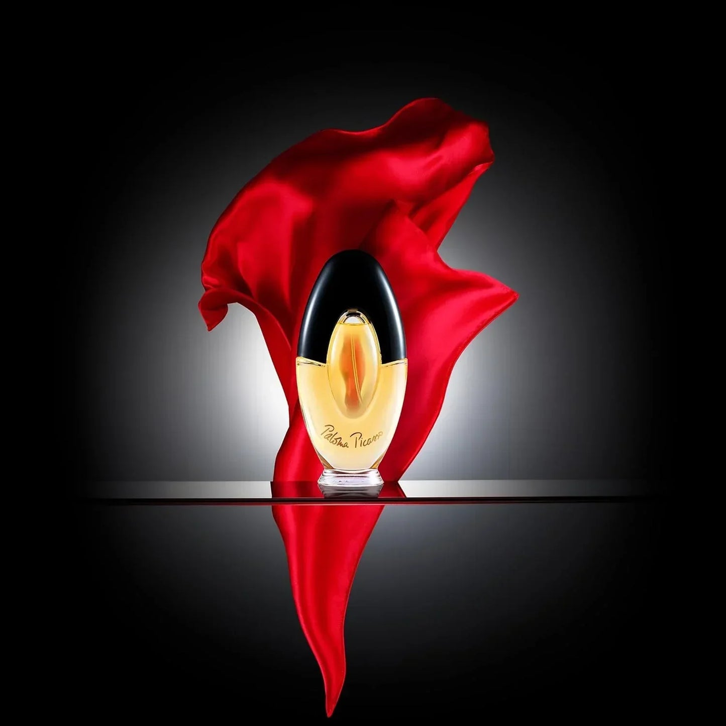 Paloma Picasso fragrance bottle with red fabric backdrop, golden liquid, black cap