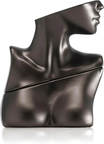 A sculptural dark metallic perfume bottle shaped like a stylized female torso and neck in a side profile, shown on a clean white background with a soft reflection. 100ml