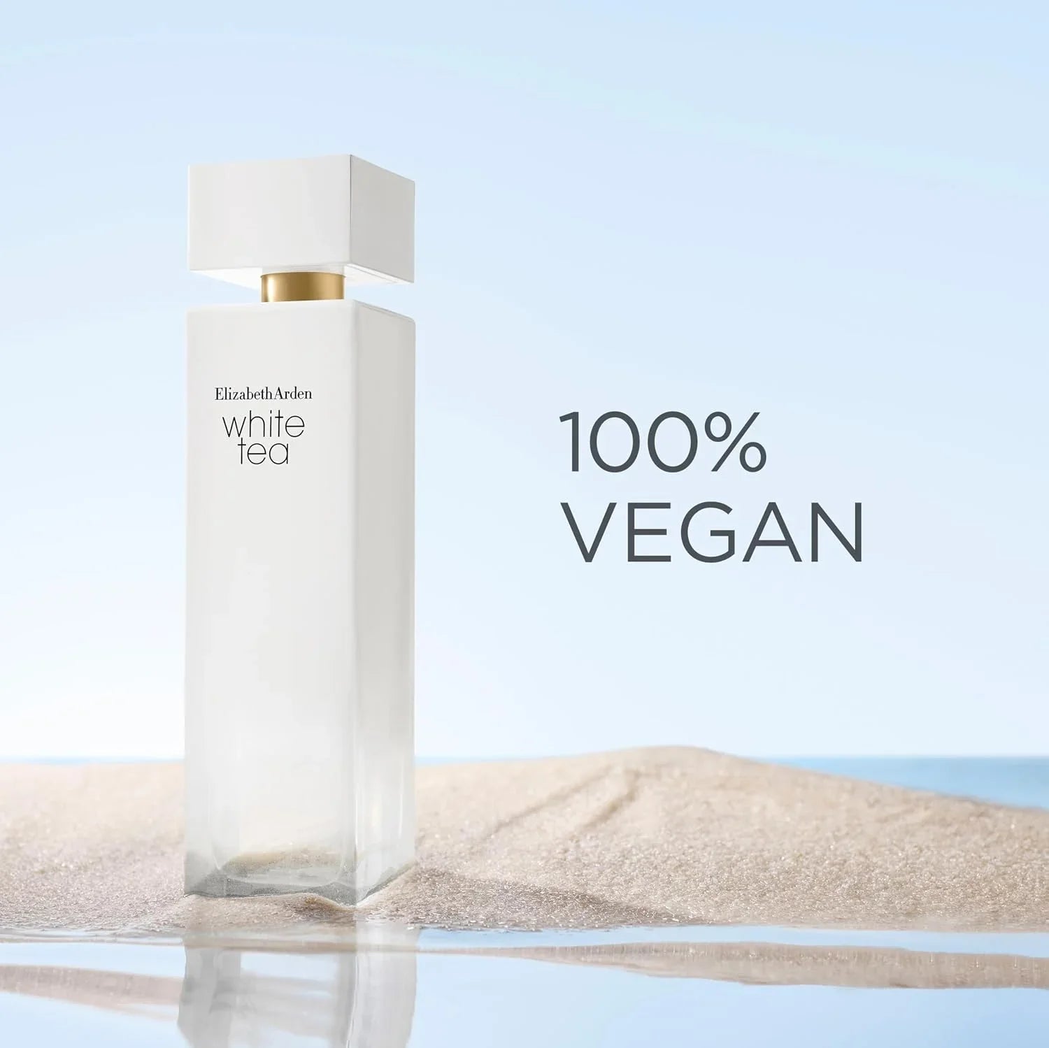 Elizabeth Arden White Tea bottle standing on sand with water reflection, next to the text '100% VEGAN' on a pale blue background.