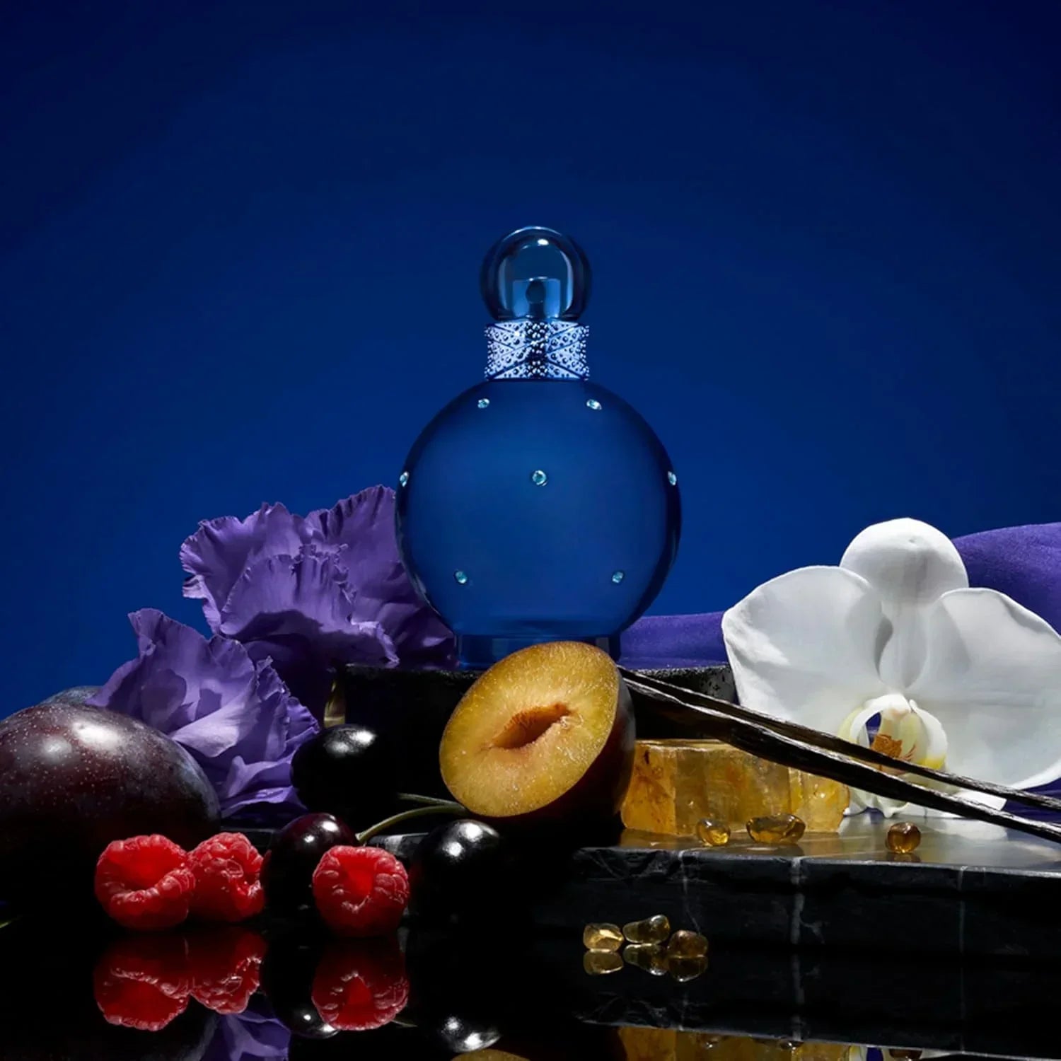 Paris Hilton Midnight Fantasy Eau de Parfum 100ml fragrance bottle with plum, raspberries, orchid on dark surface
