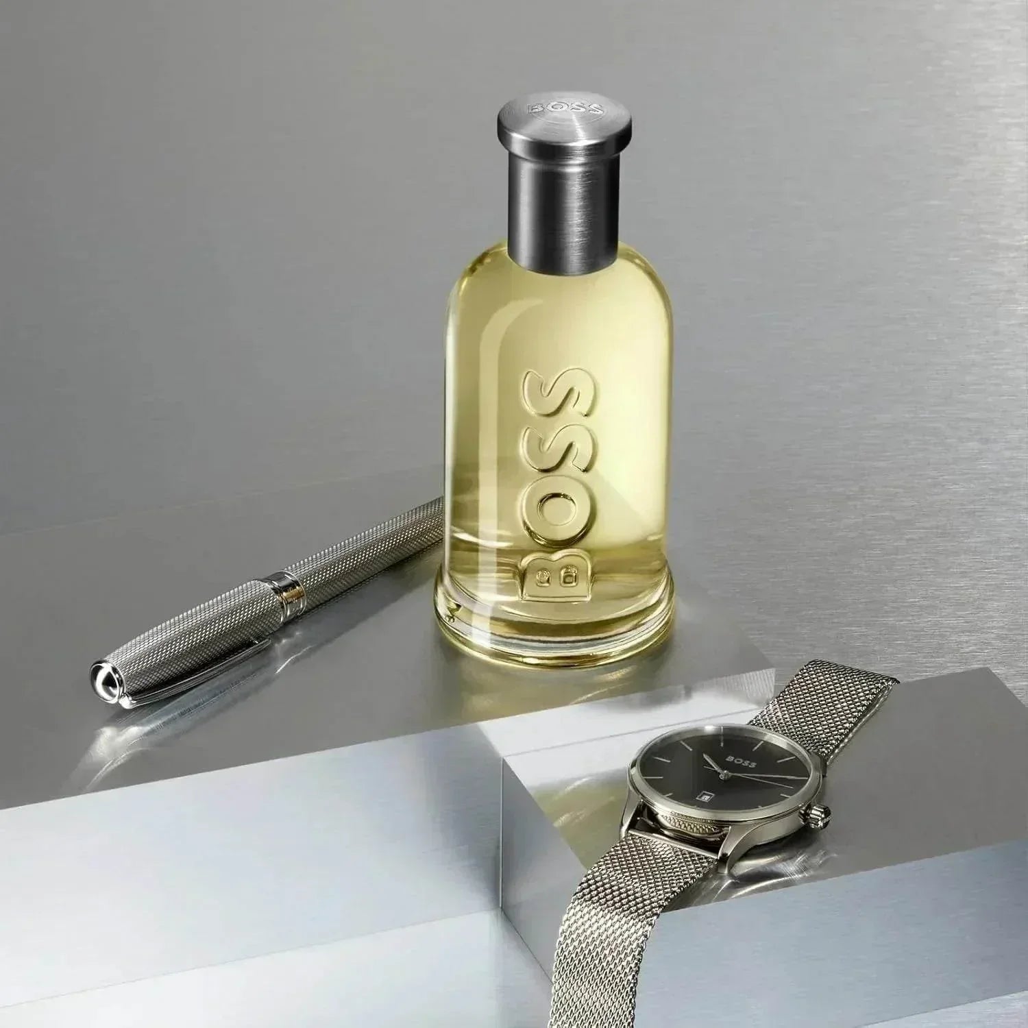 BOSS Bottled Eau de Toilette fragrance bottle with pen and watch on metallic surface