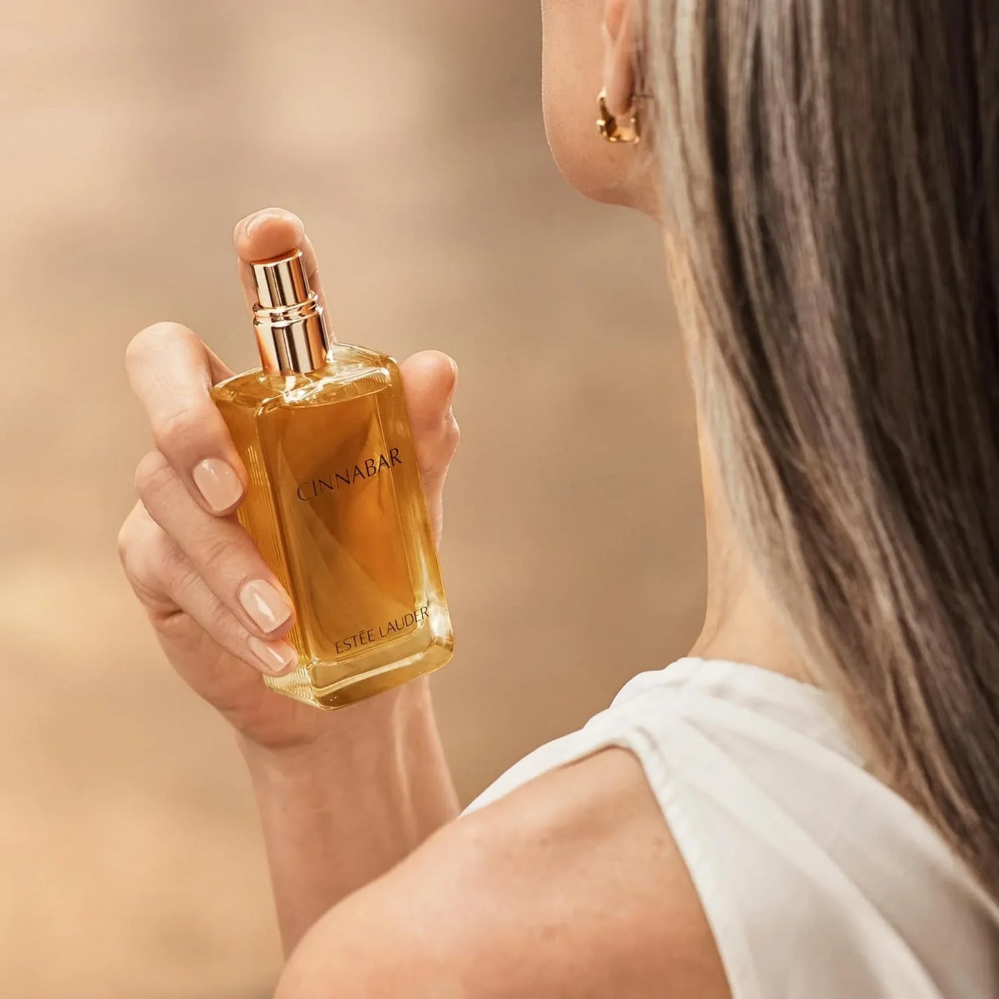 Person holding a CINNABAR Estée Lauder perfume bottle against a blurred background