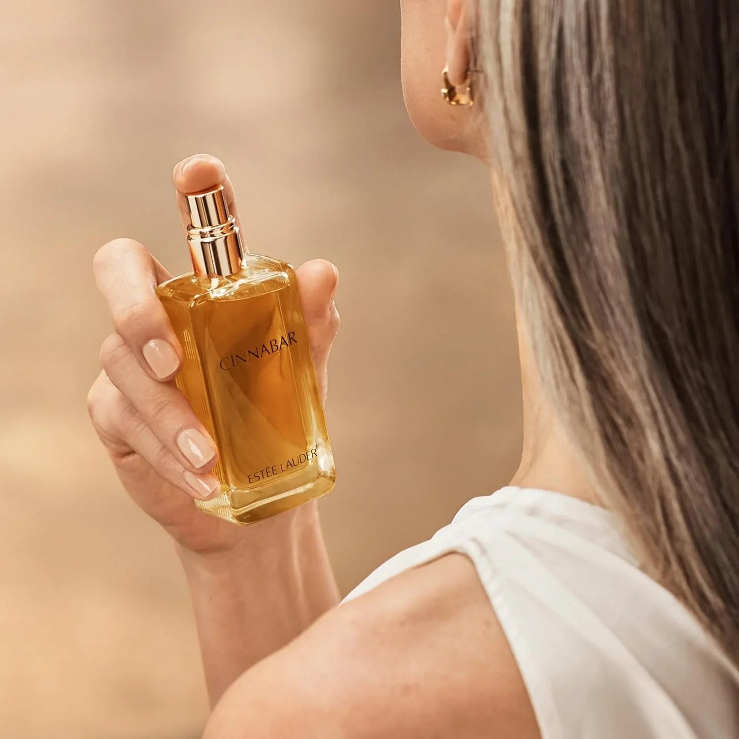 Person holding a CINNABAR Estée Lauder perfume bottle against a blurred background