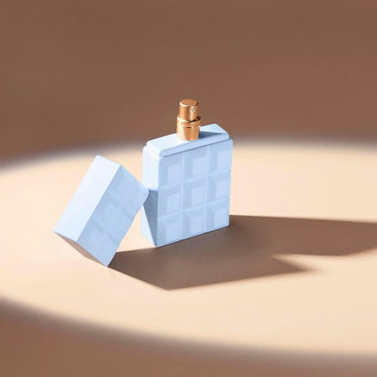 A light blue perfume bottle designed to look like a chocolate bar, with its cap leaning against it, set on a warm beige surface under a spotlight.