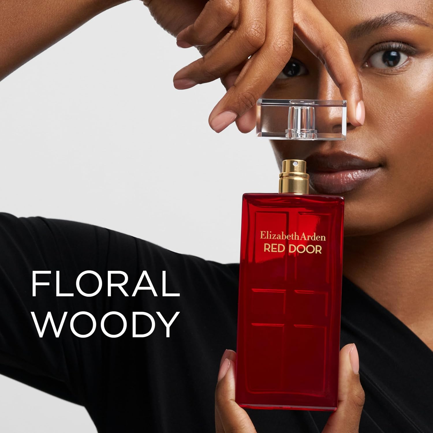 Person holding a red Elizabeth Arden perfume bottle with 'Floral Woody' description.