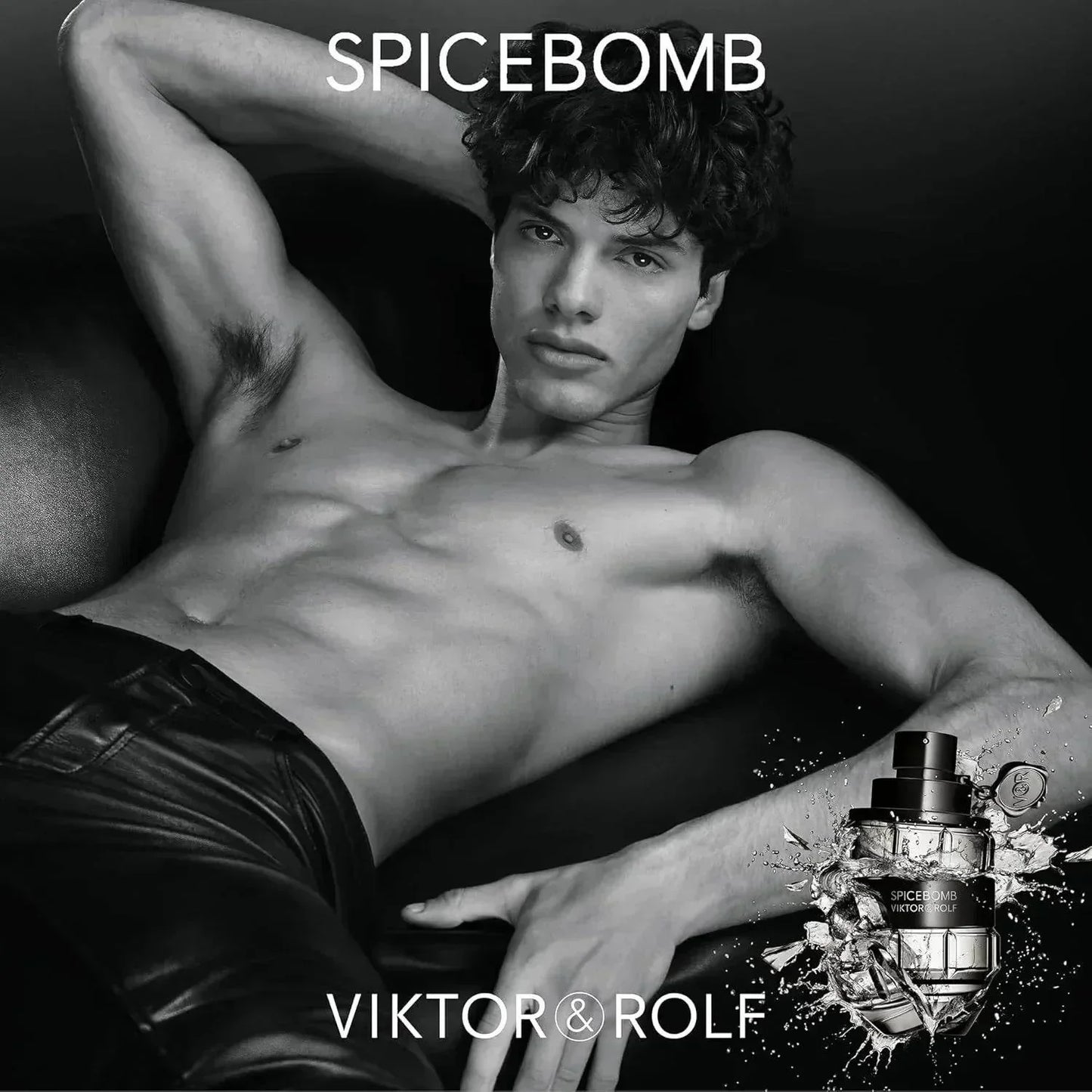 Shirtless male model reclining with Viktor & Rolf Spicebomb fragrance bottle, black and white.