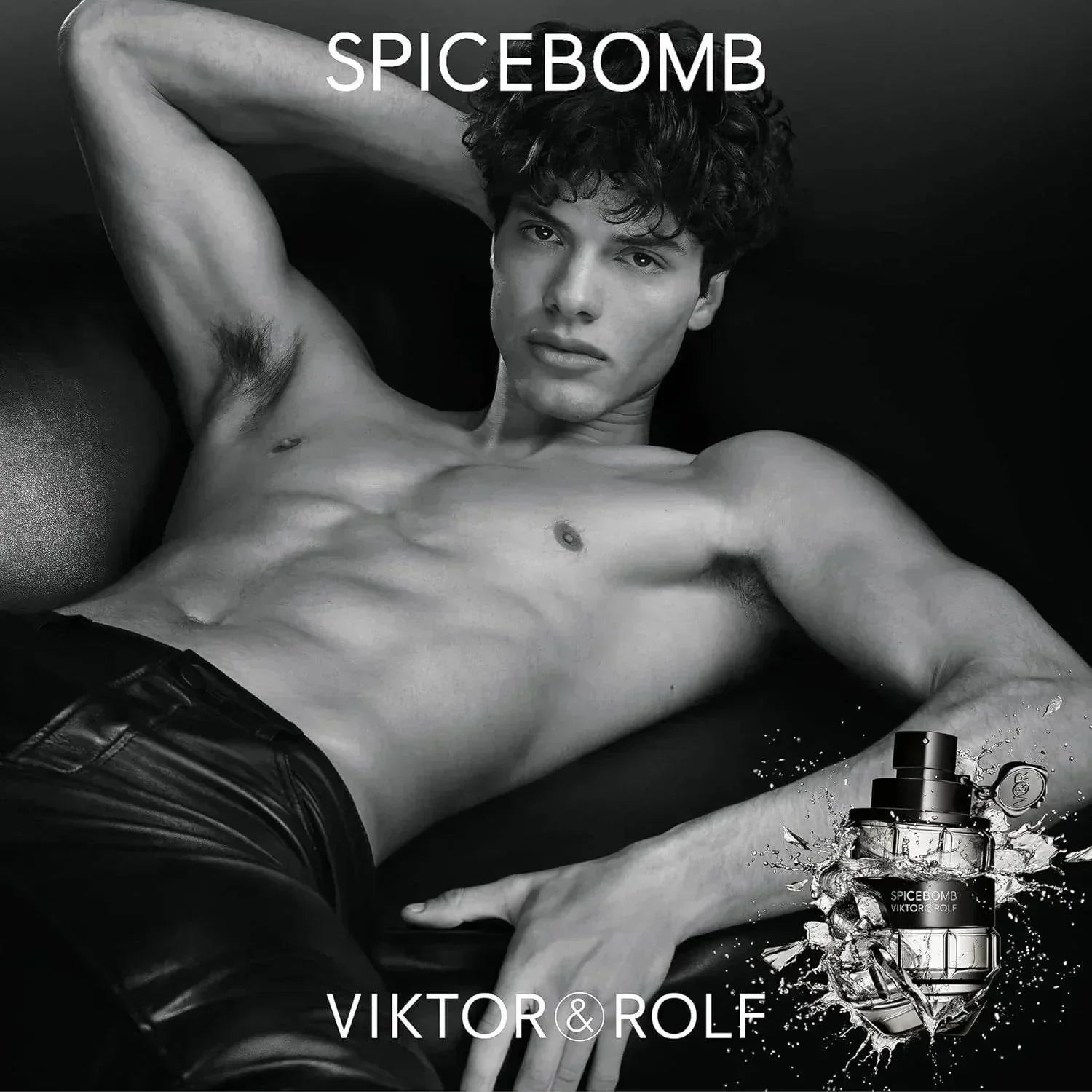 Shirtless male model reclining with Viktor & Rolf Spicebomb fragrance bottle, black and white.