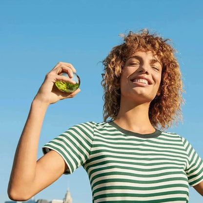 Woman holding green liquid perfume bottle outdoors under blue sky