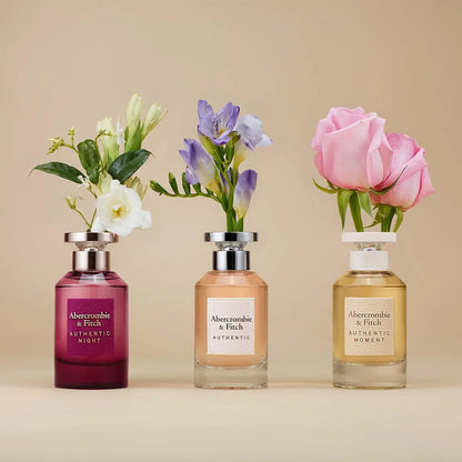 Abercrombie & Fitch Authentic Night, Authentic, and Authentic Moment fragrance bottles with floral arrangements