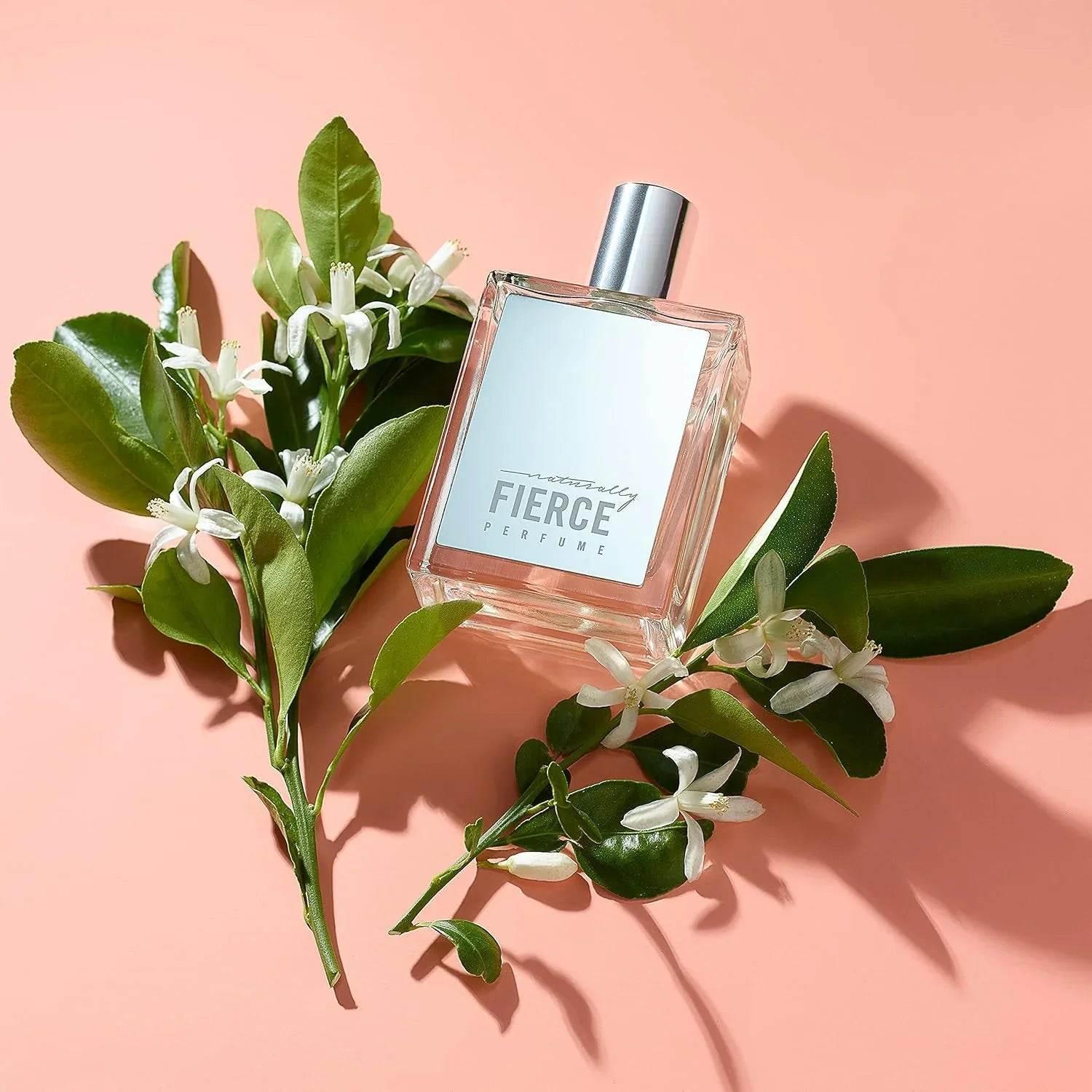 Naturally Fierce Perfume fragrance bottle with green leaves and white flowers on pink background