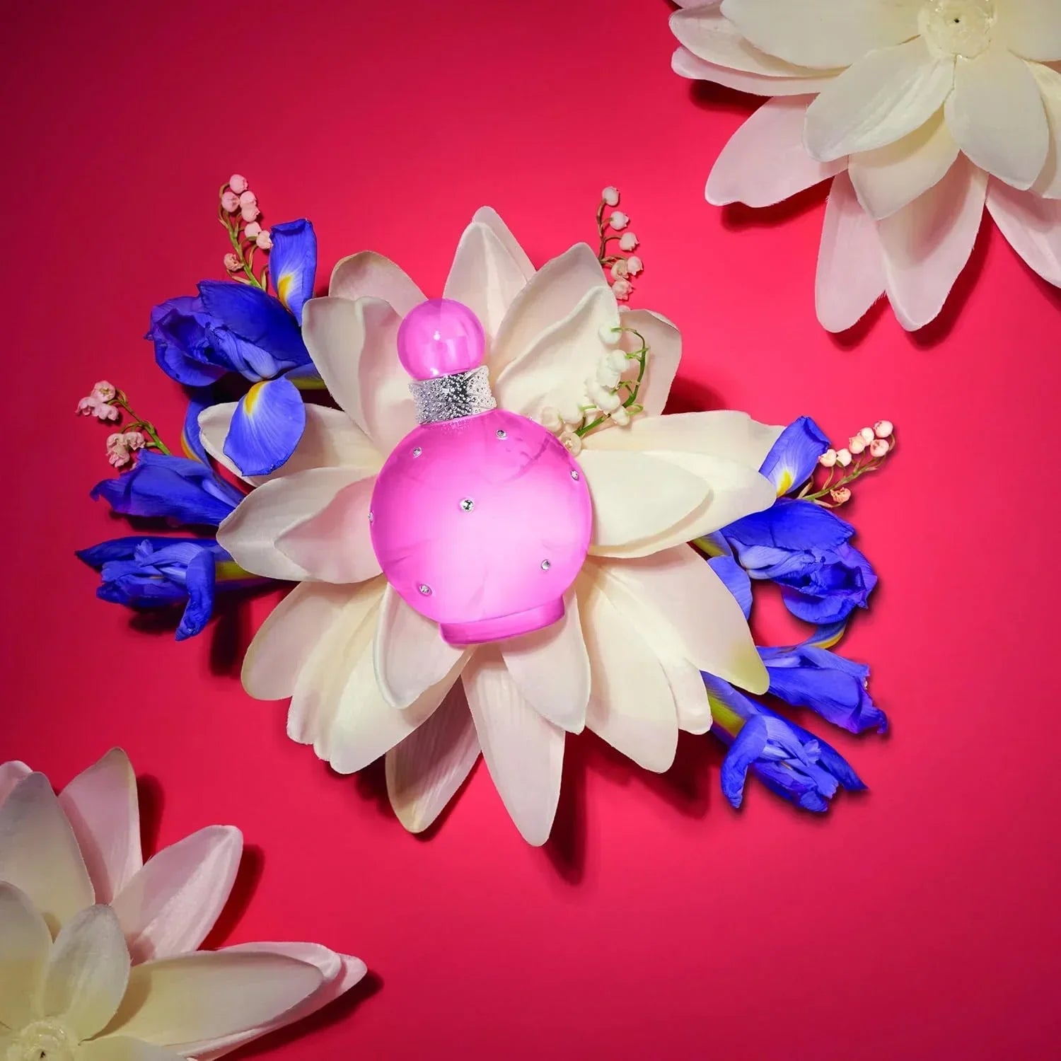 Pink perfume bottle nestled in white and blue flowers on red background