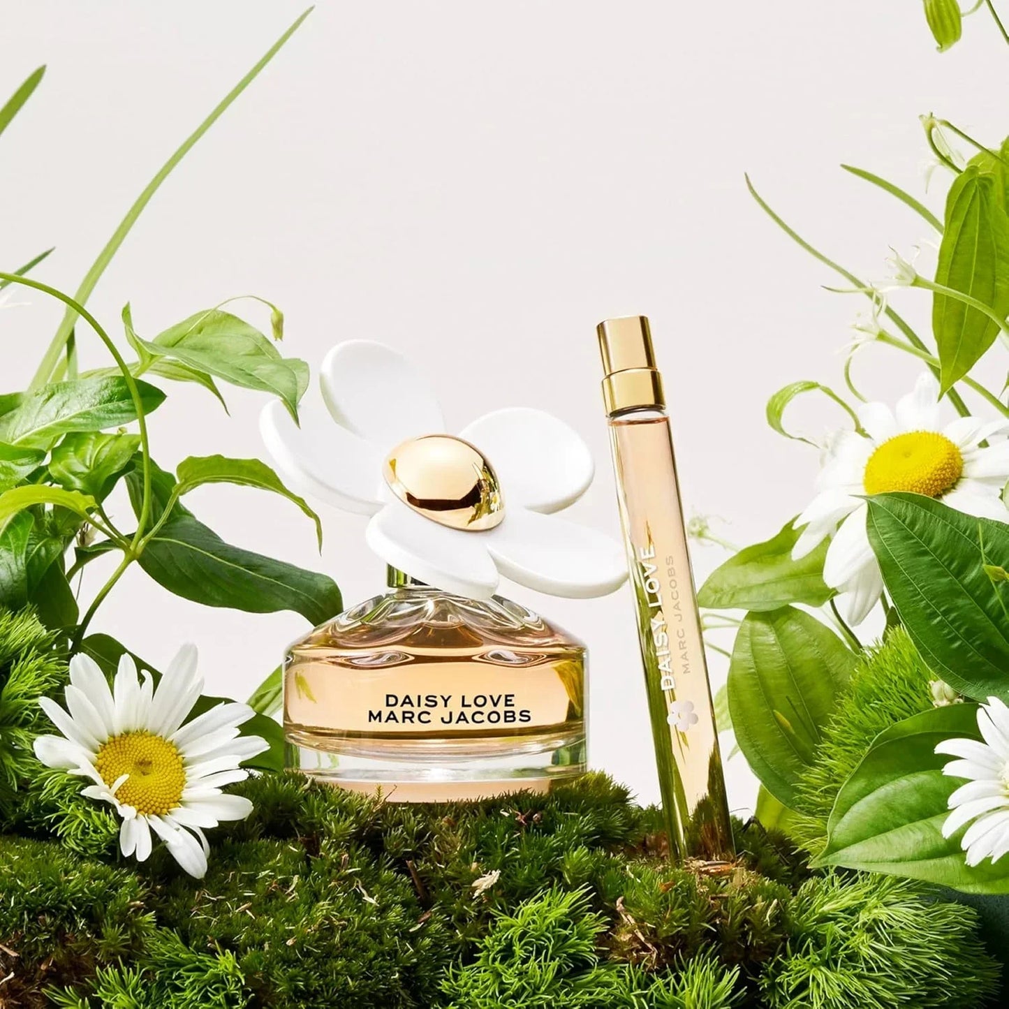 Marc Jacobs Daisy Love Eau de Toilette bottle with travel spray surrounded by daisies and greenery