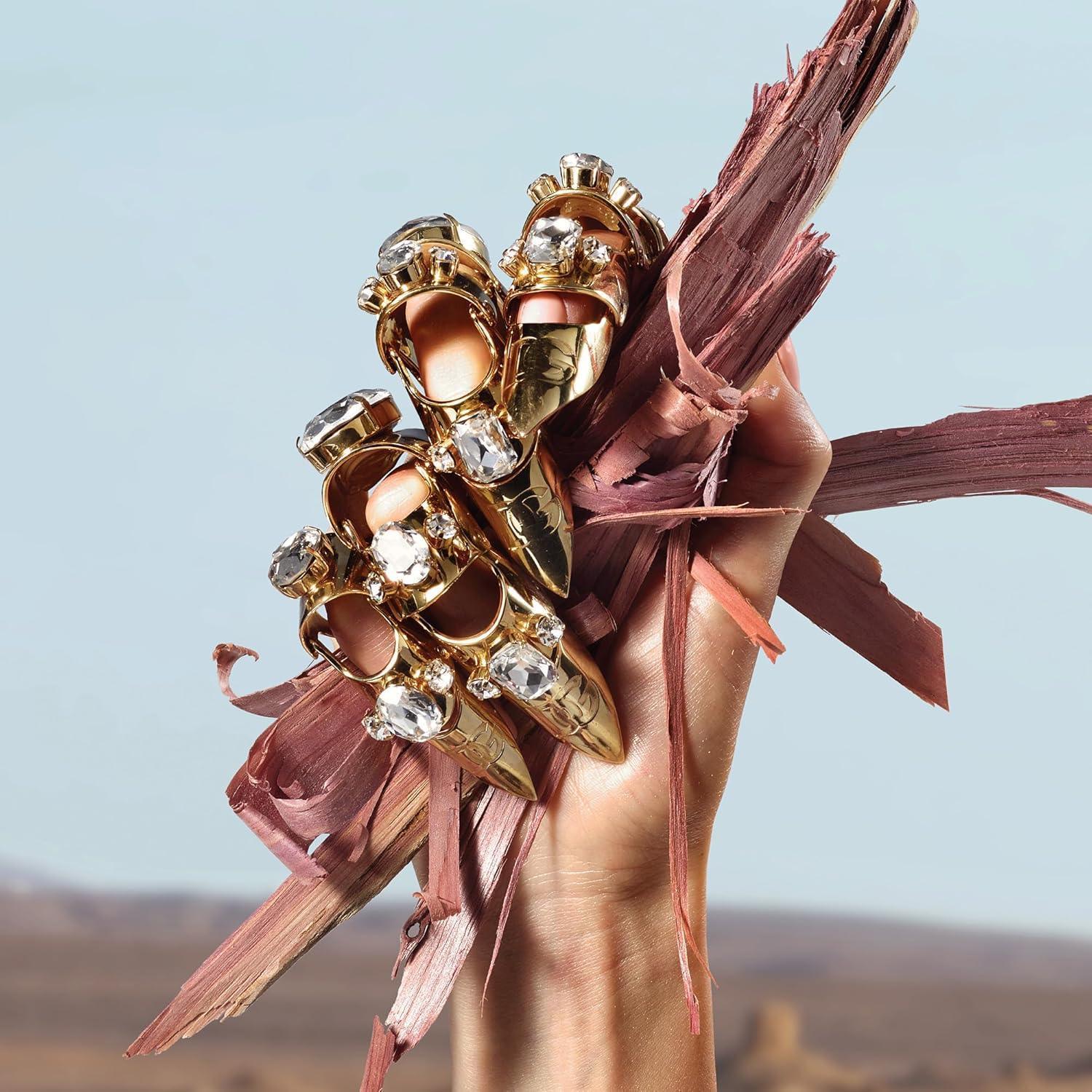 Hand holding ornate gold rings with crystals against desert backdrop