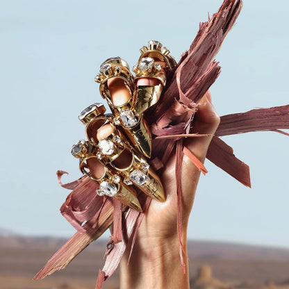 Hand holding ornate gold rings with crystals against desert backdrop