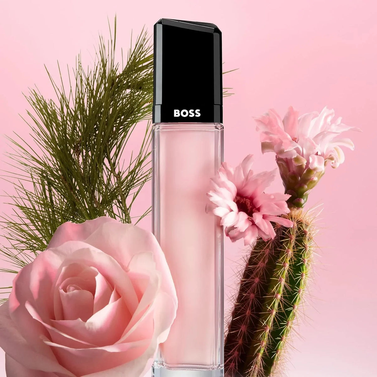 BOSS liquid lipstick in a clear rectangular tube with a black cap, styled with pink flowers and green cactus against a pink background.