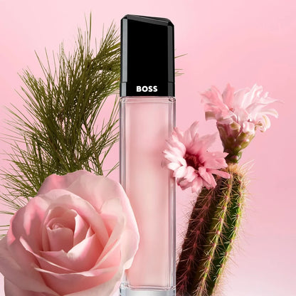 BOSS liquid lipstick in a clear rectangular tube with a black cap, styled with pink flowers and green cactus against a pink background.