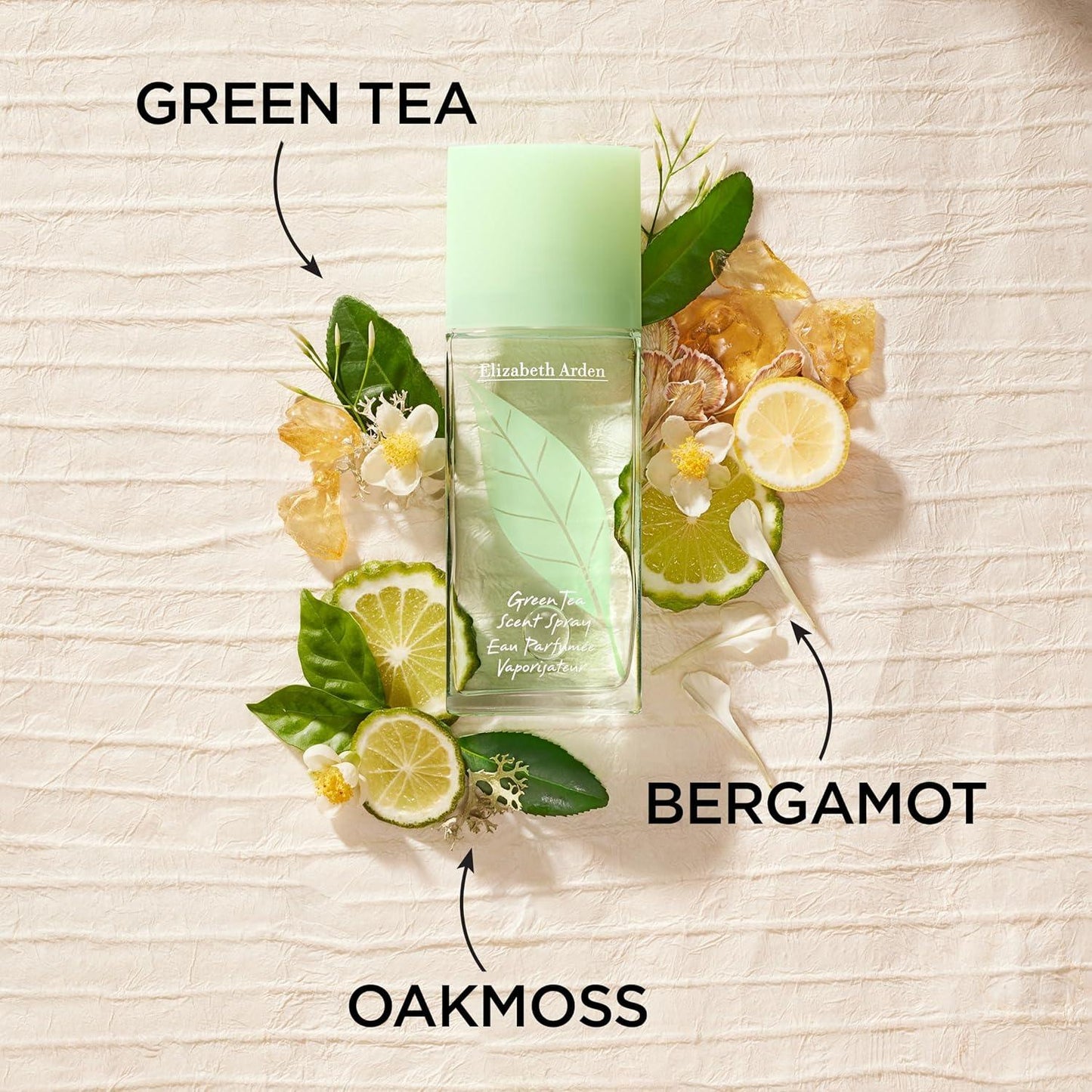 Elizabeth Arden Green Tea perfume bottle with green tea leaves, bergamot slices, and oakmoss on a textured beige background.