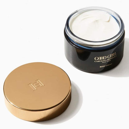 A jar of Carolina Herrera Good Girl Body Cream shown open with the white cream visible, alongside its metallic gold screw-on lid on a clean white background.