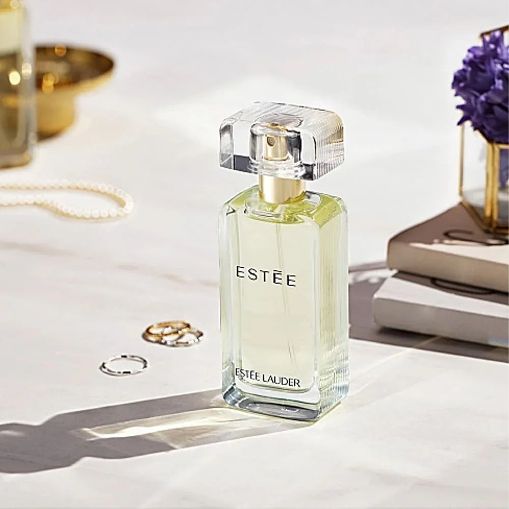 Estée Lauder perfume bottle on a white surface with jewelry and books in the background