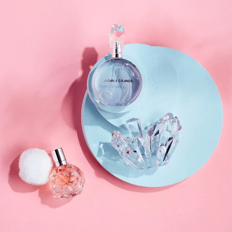 Two perfume bottles on a pink background with a blue circular tray and crystal-like object.