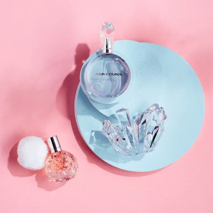 Two perfume bottles on a pink background with a blue circular tray and crystal-like object.