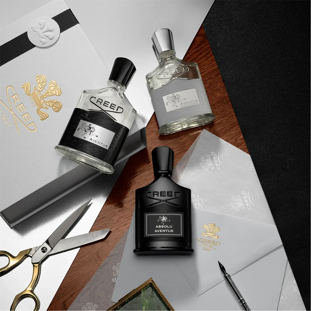 Three Creed perfume bottles on a wooden surface with a gold scissors and pen.