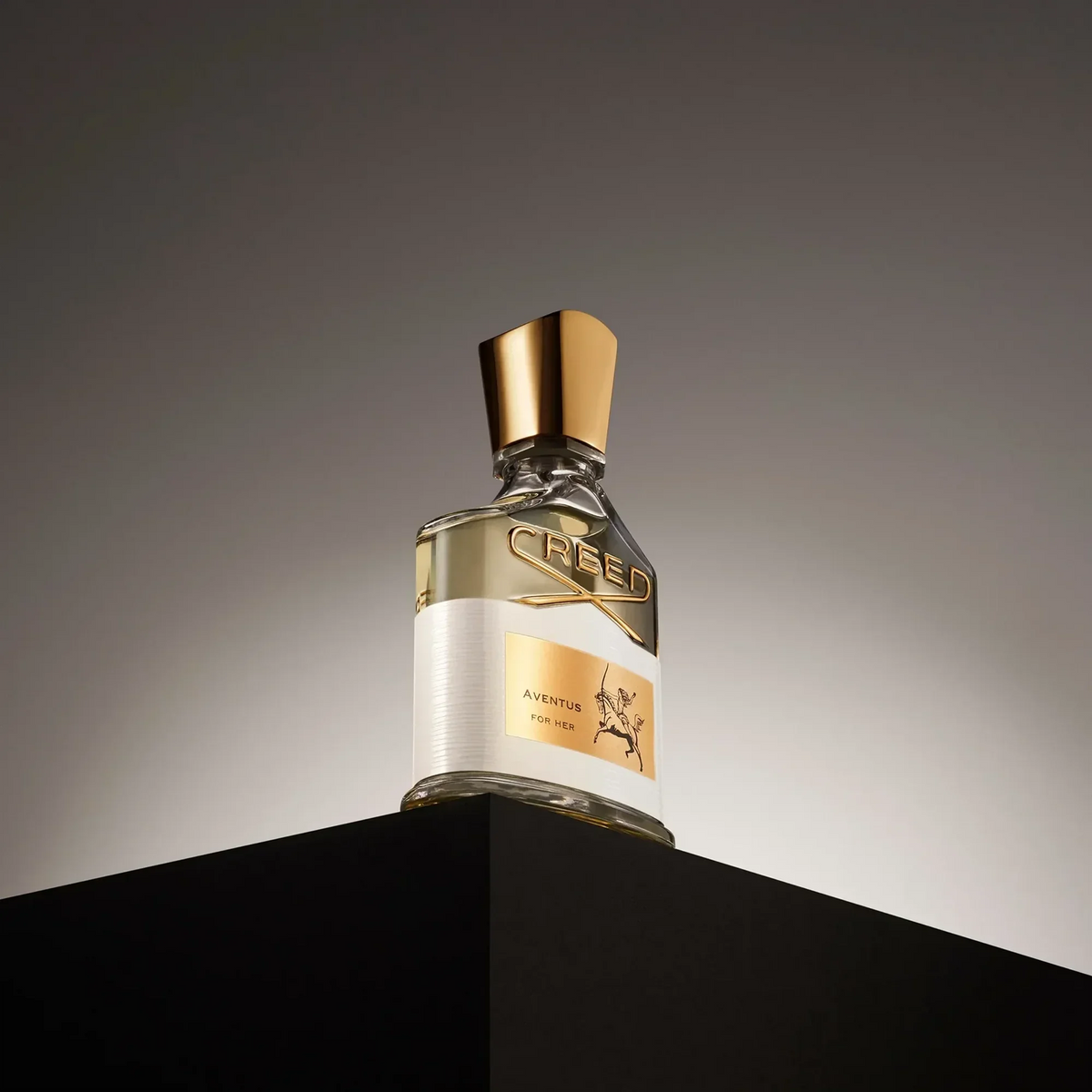 Creed perfume bottle with gold cap on a black and gray background
