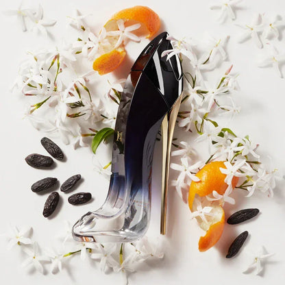 High heel perfume bottle with white flowers, orange peels, and tonka beans on white background