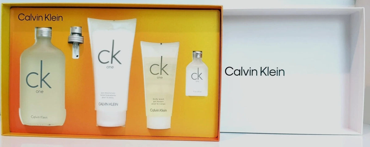 Calvin Klein One One fragrance gift set featuring a frosted glass bottle, a tube, a cream tube, and a small spray bottle, displayed in an orange box next to an open white box with Calvin Klein branding.