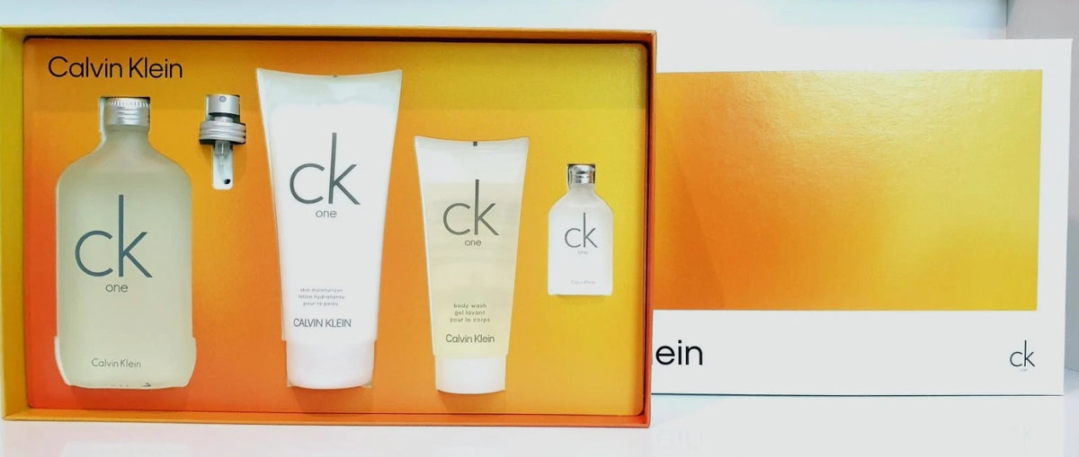 Calvin Klein One fragrance gift set with a glass bottle, spray atomizer, lotion tube, body wash tube, and a smaller bottle, displayed in an orange box alongside a branded card.